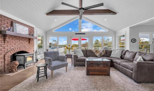 Great room w/ cathedral ceilings & exposed wooden beams, brick fireplace w/ Hearthstone wood burning cast iron stove, shiplap ceiling, and large gable window for natural light