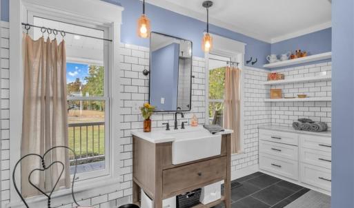 Primary en-suite bathroom w/ farmhouse vanity w/ quartz countertop, frameless glass door and floor-to-ceiling tile shower, built in dresser vanity, & large deep wall closet