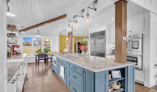 4-chair breakfast island w/ wood columns and display shelves, pantry cabinet w/ pull-out drawers, under cabinet lighting, and cathedral and vaulted shiplap ceilings w/ suspended beams