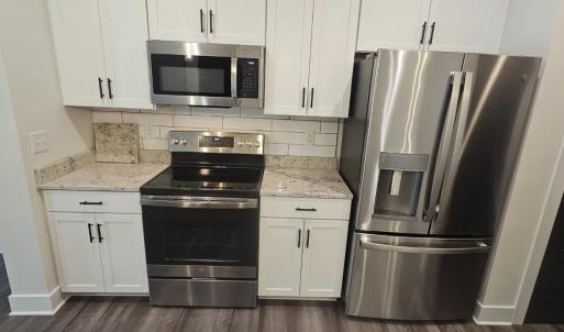 Stainless steel appliances include microwave, refrigerator, glass surface range .Also showing granite countertops and ceramic tile backsplash ,pantry closet to right
