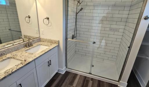 Primary bedroom w/ ensuite bath w/ floor to ceiling ceramic tiled shower , glass doors, linen shelves, & a double undermount sink granite topped vanity