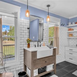 Primary en-suite bathroom w/ farmhouse vanity w/ quartz countertop, frameless glass door and floor-to-ceiling tile shower, built in dresser vanity, & large deep wall closet