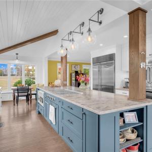 4-chair breakfast island w/ wood columns and display shelves, pantry cabinet w/ pull-out drawers, under cabinet lighting, and cathedral and vaulted shiplap ceilings w/ suspended beams