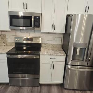 Stainless steel appliances include microwave, refrigerator, glass surface range .Also showing granite countertops and ceramic tile backsplash ,pantry closet to right