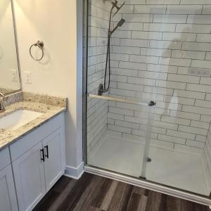 Primary bedroom w/ ensuite bath w/ floor to ceiling ceramic tiled shower , glass doors, linen shelves, & a double undermount sink granite topped vanity